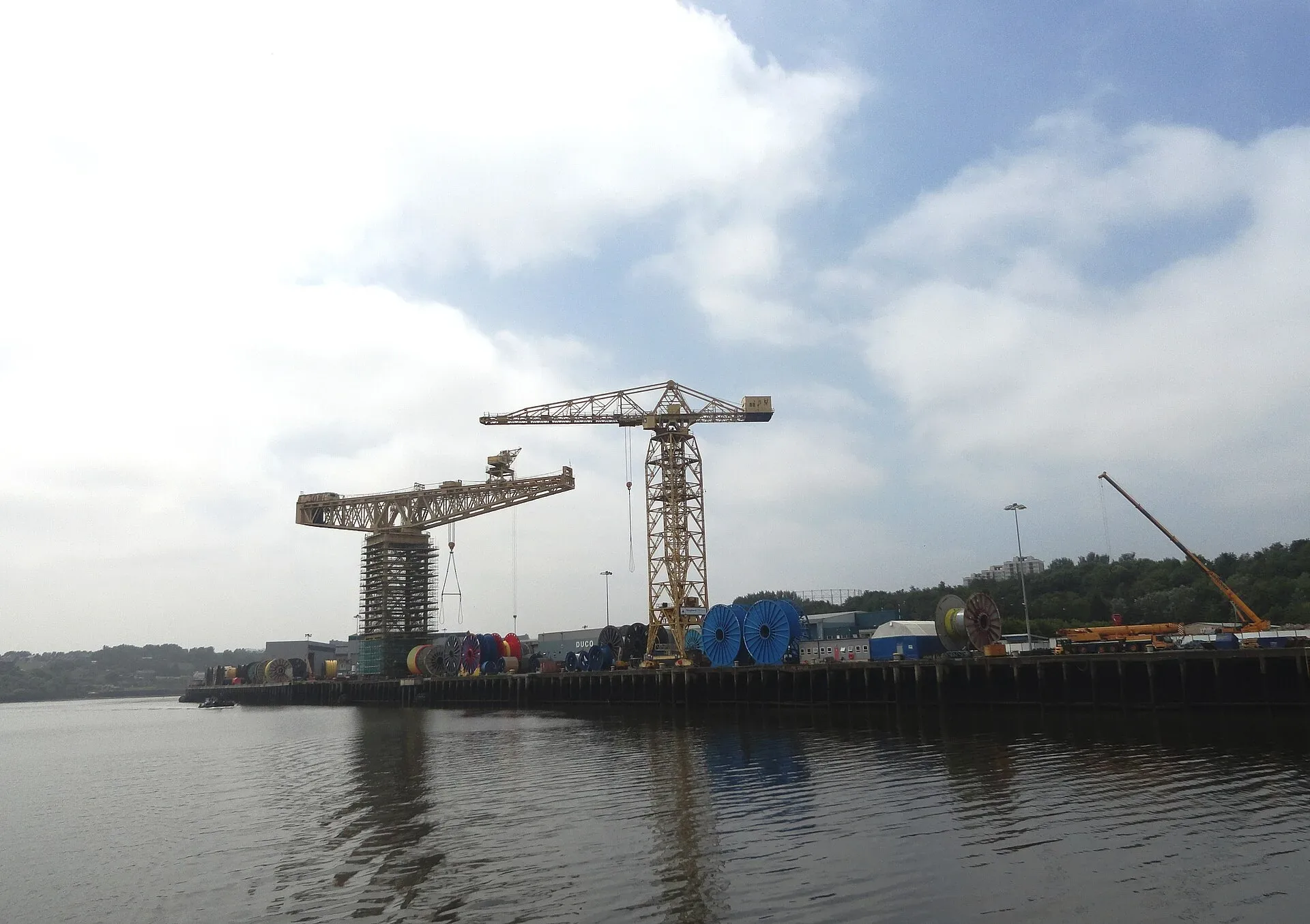 Former shipyard cranes beside a river under a cloudy sky