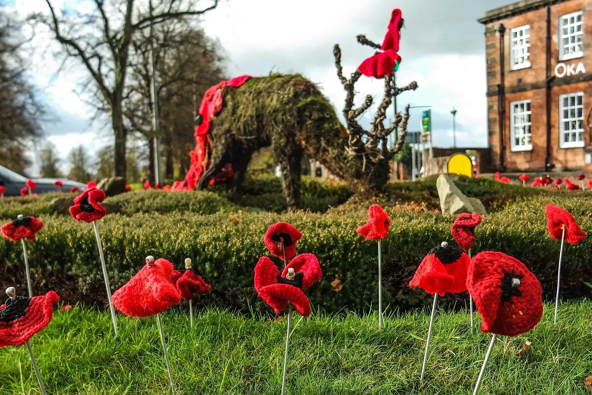 Red knitted poppies planted in a flower bed beside a topiary display