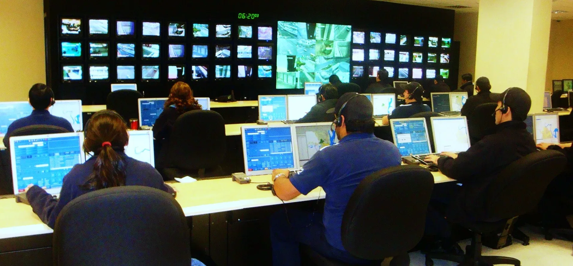 Call handlers at desks in front of a wall of screens in an emergency control room