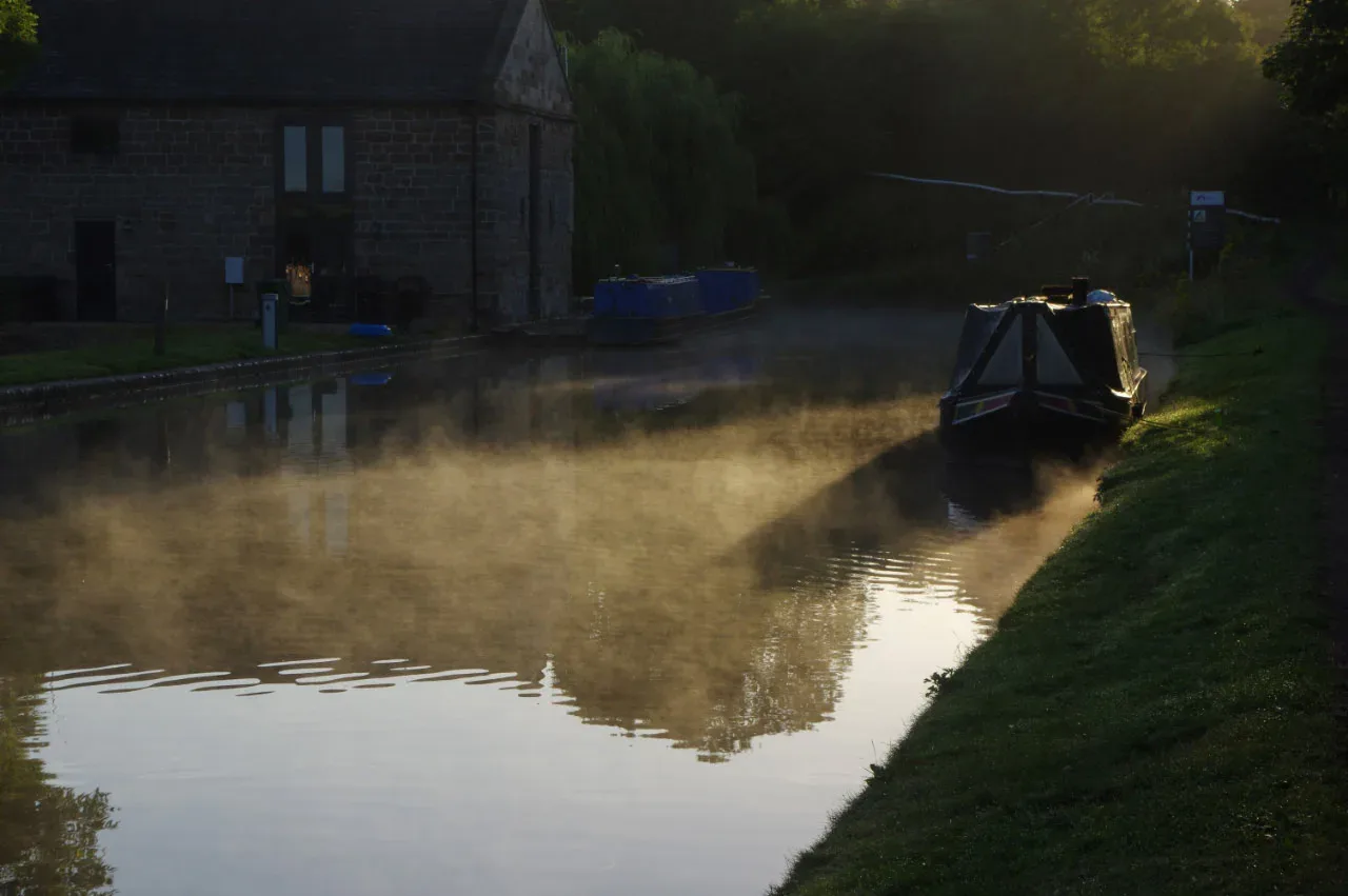 Morning mist rising off a canal beside a moored narrowboat