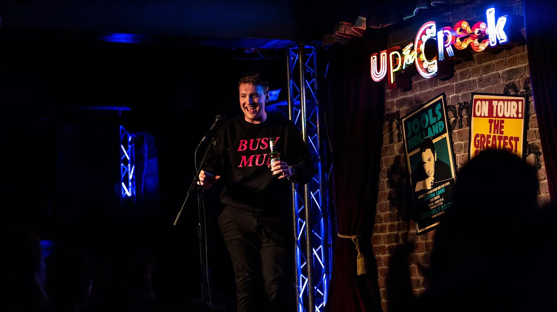 Joe Lycett performing stand-up comedy on a small stage