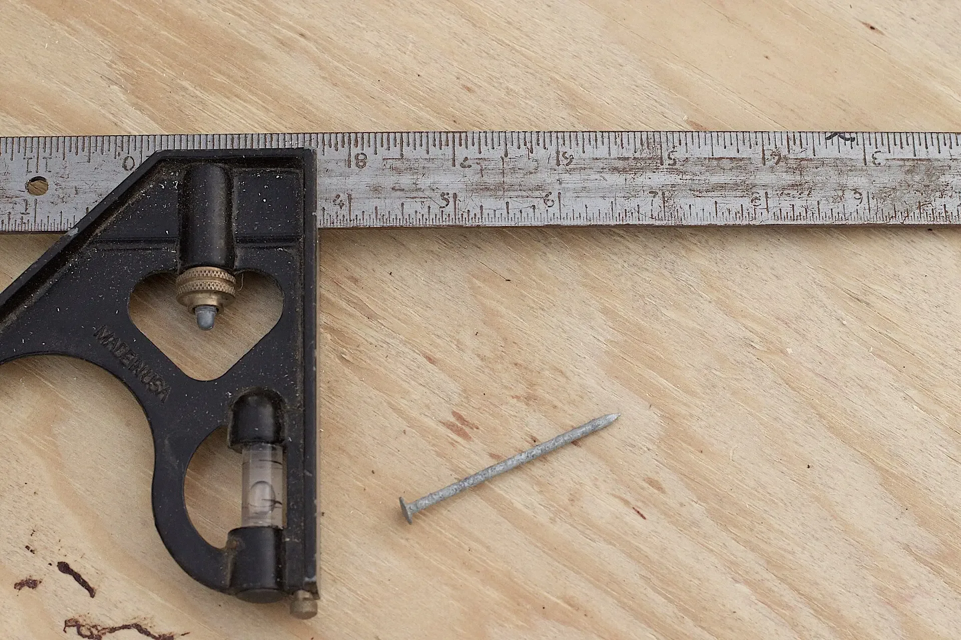 A metal square, ruler and nail on a wooden workbench