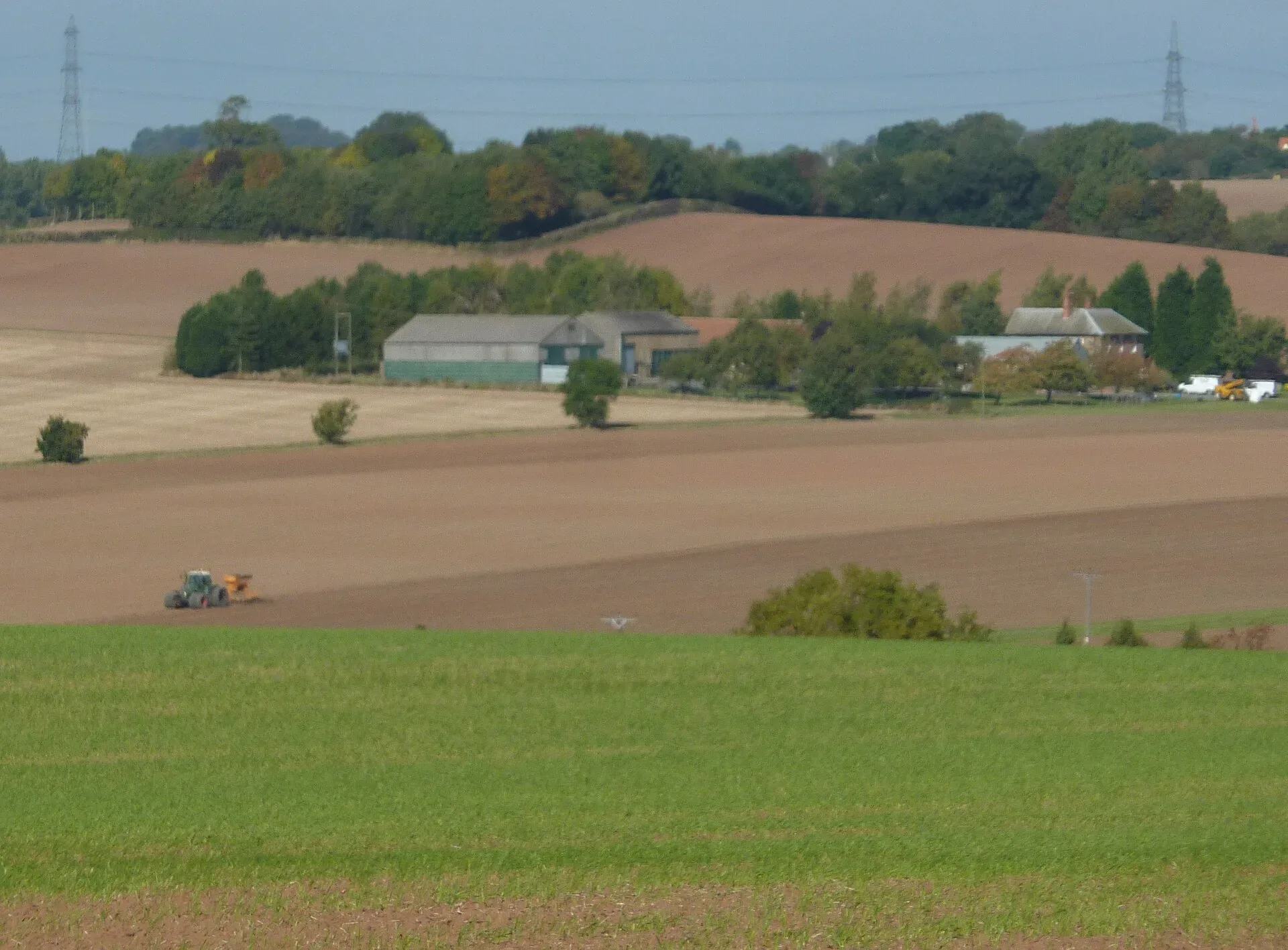 A tractor working in a ploughed field below a farmhouse in the English countryside